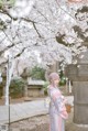 A woman in a pink kimono standing in front of a tree.